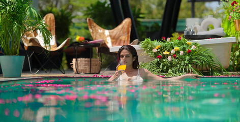Indian Asian Hindu gen z woman bathing rose petals water park pool edge resort hold glass drink...