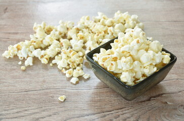 salty popcorn spreading from black bowl on wooden table 