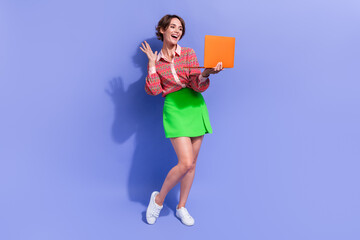 Full length photo of cheerful pretty girl wear stylish shirt green skirt say hello on laptop webcam isolated on blue color background