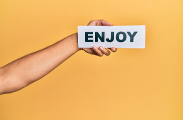 Hand of caucasian man holding paper with enjoy word over isolated yellow background