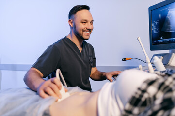 A male doctor performs an abdominal ultrasound on a female patient in the clinic. Pregnant woman at a gynecologist's appointment. - obrazy, fototapety, plakaty