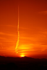 山に沈む夕日と登り龍の飛行機雲