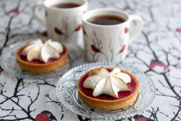 Tartlet cake with meringue and cups of tea on the table. Bullfinch pattern on tablecloths and cups....