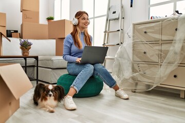 Young caucasian woman using laptop and headphones sitting with dog at new home