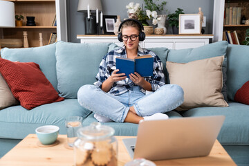 Obraz premium Young religious woman is sitting at home, happy because she found faith while reading books about religion. Believer female enjoying her time knowing about God.