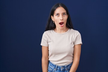 Young hispanic woman standing over blue background angry and mad screaming frustrated and furious,...