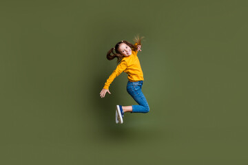 Full length photo of nice kid with ponytails hairdo dressed yellow sweatshirt jumping in empty space isolated on khaki color background