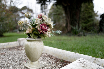 Faded and dirty artificial flowers seen in a marble vase on the site of a large grave in rural...