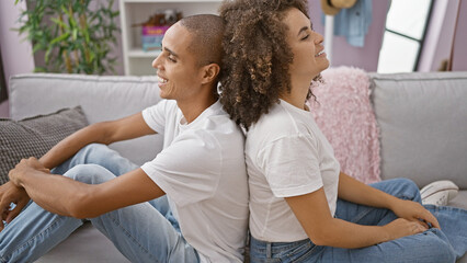 Obraz premium Smiling beautiful couple sitting back-to-back on sofa, enjoying each other's company in their cosy home