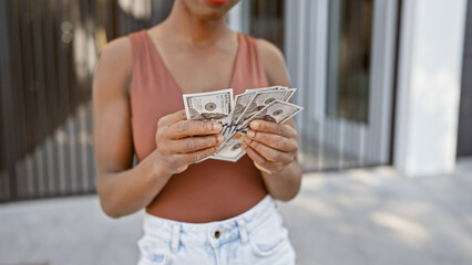 Attractive african american woman brimming with joy, counting handfuls of dollar bills on an urban...