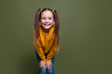Portrait of adorable small kid with tails dressed yellow sweatshirt hands on knees smiling to you isolated on khaki color background