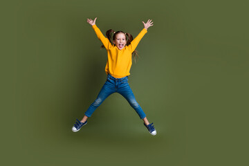 Full length photo of good mood kid with ponytails hairdo dressed yellow shirt flying raising hands up isolated on khaki color background
