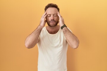 Fototapeta na wymiar Middle age man with beard standing over yellow background with hand on head, headache because stress. suffering migraine.