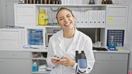 Young beautiful hispanic woman scientist using smartphone smiling at laboratory