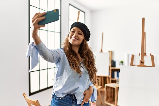 Young beautiful hispanic woman artist make selfie by smartphone at art studio