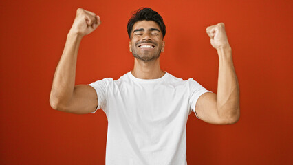Handsome young hispanic man celebrating triumphantly against a vibrant red background