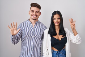 Young hispanic couple standing over white background showing and pointing up with fingers number nine while smiling confident and happy.