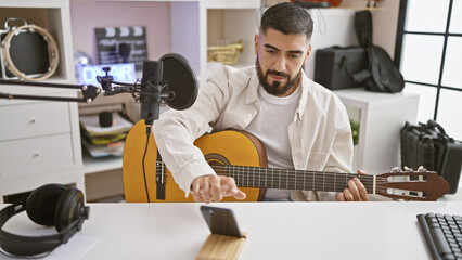 Handsome man recording acoustic guitar music in a modern indoor studio setup, showcasing creativity...