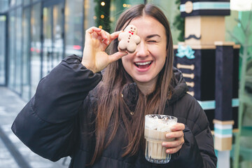 A young woman drinks coffee with a gingerbread boy in a cafe on the street.