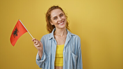 Smiling caucasian woman holding an albanian flag against a yellow backdrop, conveying national...