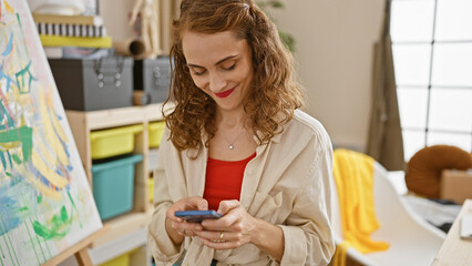 Confident young woman artist captured smiling as she effortlessly engages with her smartphone while...