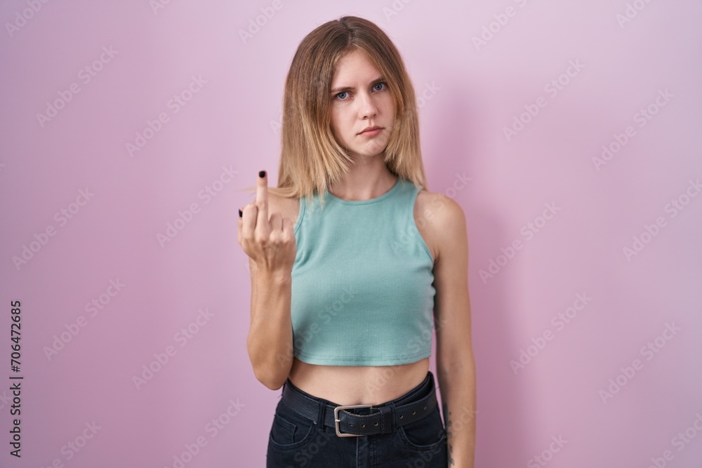 Poster blonde caucasian woman standing over pink background showing middle finger, impolite and rude fuck o