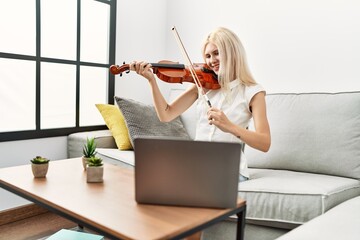Young blonde woman musician smiling confident having online violin lesson at home