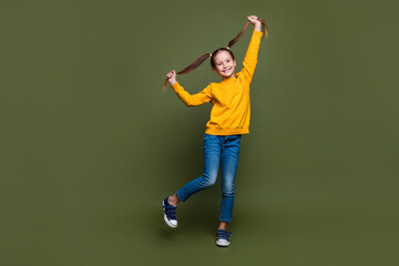 Full size photo of positive schoolgirl hold ponytails wear yellow pullover denim pants having fun...
