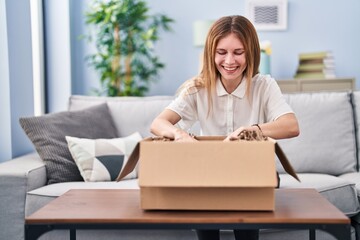 Young blonde woman unpacking cardboard box at home