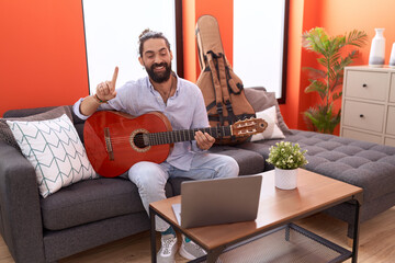 Hispanic man with beard playing classic guitar at home smiling with an idea or question pointing finger with happy face, number one