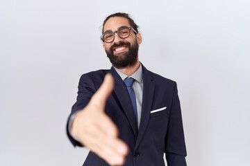 Hispanic man with beard wearing suit and tie smiling friendly offering handshake as greeting and welcoming. successful business.
