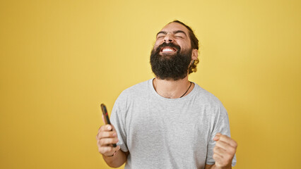 Joyful bearded man laughs holding comb isolated on yellow background