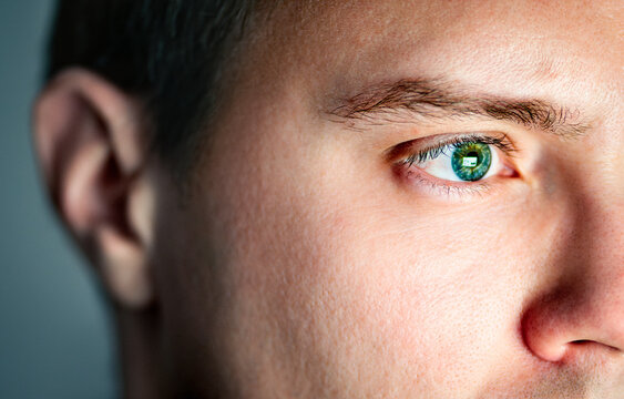 Eye and ear. See and hear. Senses concept. Skin with pore. Closeup of face of a man. Computer screen light reflect from green eye. Deaf person or bad eyesight. Autism or adhd. Sound and sight health.
