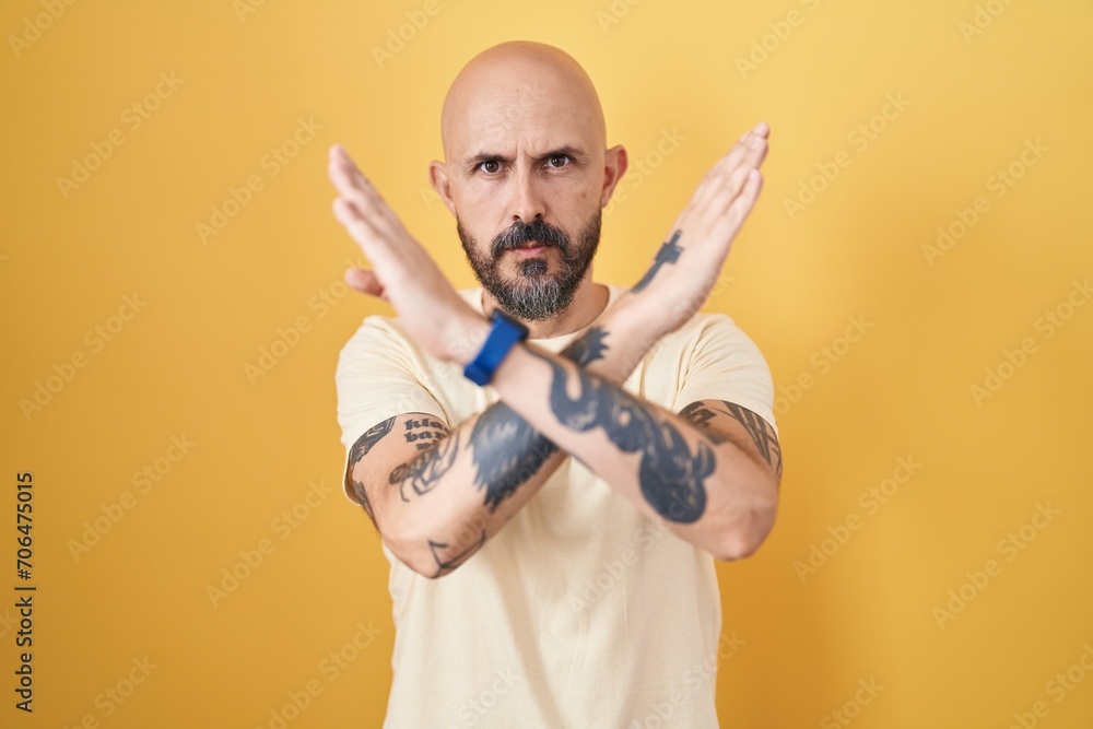 Wall mural Hispanic man with tattoos standing over yellow background rejection expression crossing arms doing negative sign, angry face