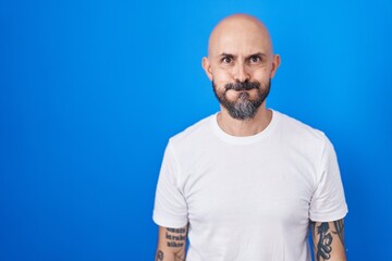 Hispanic man with tattoos standing over blue background puffing cheeks with funny face. mouth inflated with air, crazy expression. - obrazy, fototapety, plakaty