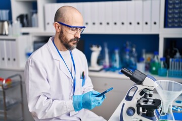 Young bald man scientist using smartphone at laboratory