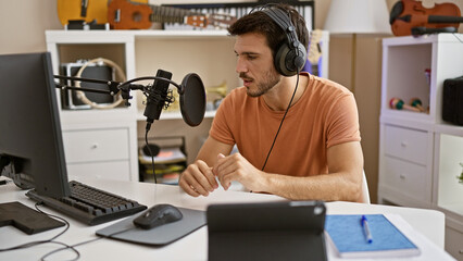 Hispanic man with headphones speaks into microphone in home studio setting, portraying a creative...