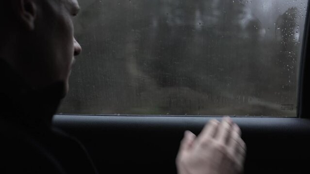 bald man is riding in the passenger seat of car on a rainy gloomy day and looking out the window
traveling by taxi or hitchhiking in the rain.close-up of a man's hand wiping a fogged-up window in car