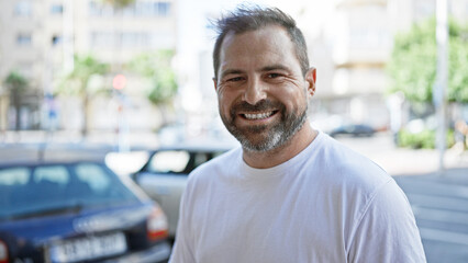 A smiling hispanic mature man with grey hair standing on a city street.