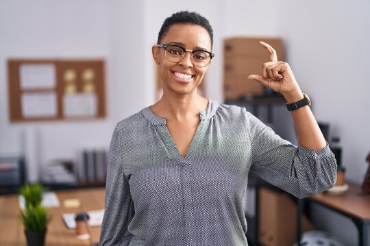 African american woman working at the office wearing glasses smiling and confident gesturing with hand doing small size sign with fingers looking and the camera. measure concept.