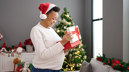 Obraz na płótnie Canvas Young pregnant woman celebrating christmas unpacking gift at home