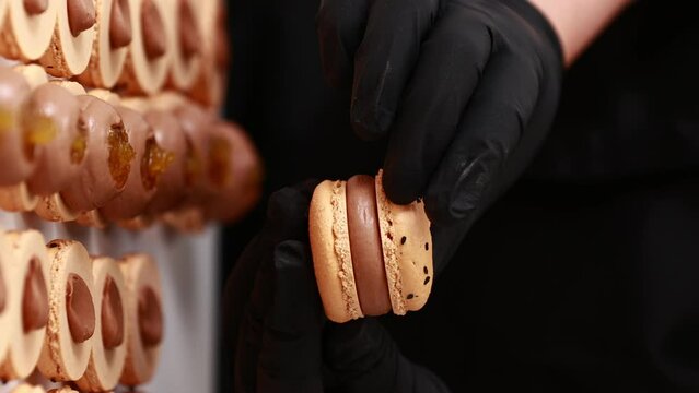 Process of making macarons macaroons, french dessert. chef hands in black gloves are assembling, connecting of two halves with chocolate stuffing at pastry shop. cooking, food and baking concept