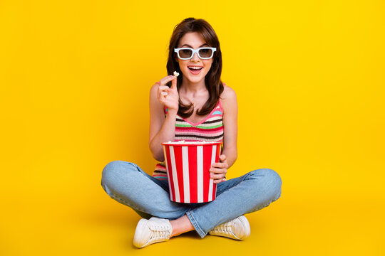 Full size photo of impressed woman dressed knitwear top in 3d glasses sit eat popcorn at home cinema isolated on yellow color background