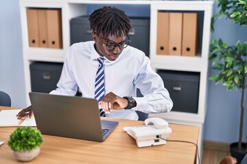 African american man business worker using laptop looking watch at office