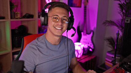 Smiling young hispanic man wearing headphones in a vibrant gaming room at night.