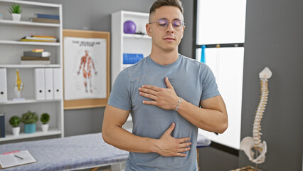 A young hispanic man with eyes closed taking a deep breath indoors at a clinic, creating a sense of health and wellbeing.