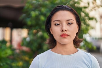 Young hispanic woman standing with serious expression at street