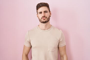 Fototapeta premium Hispanic man with beard standing over pink background looking at the camera blowing a kiss on air being lovely and sexy. love expression.