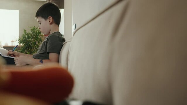 Little boy writing homework on sofa at home. Kid learing and writing alphabet.