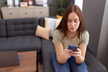 Young beautiful woman using smartphone with serious expression at home